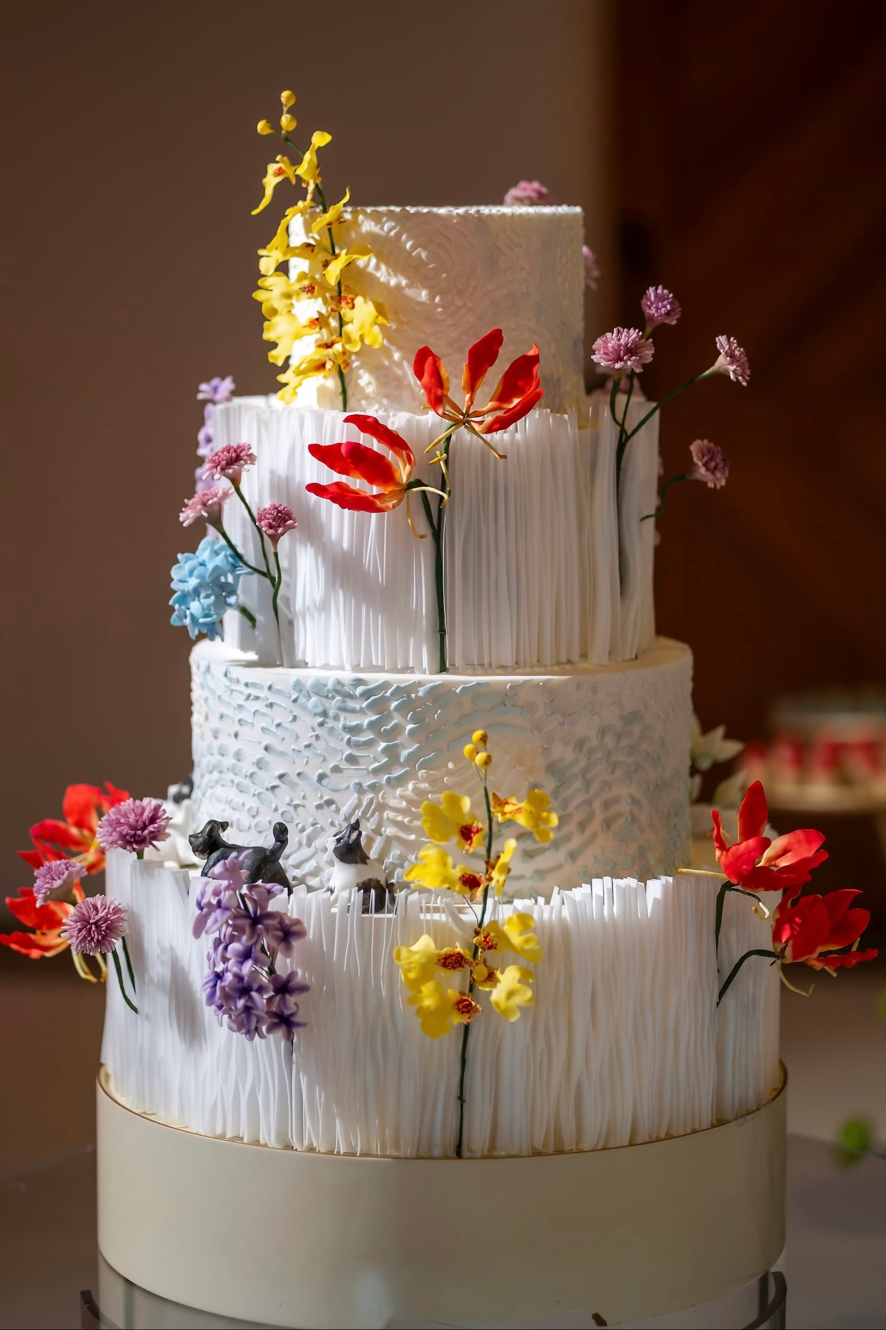 Bolo de casamento de quatro andares em branco, com texturas modeladas e flores de açúcar coloridas atravessando os andares
