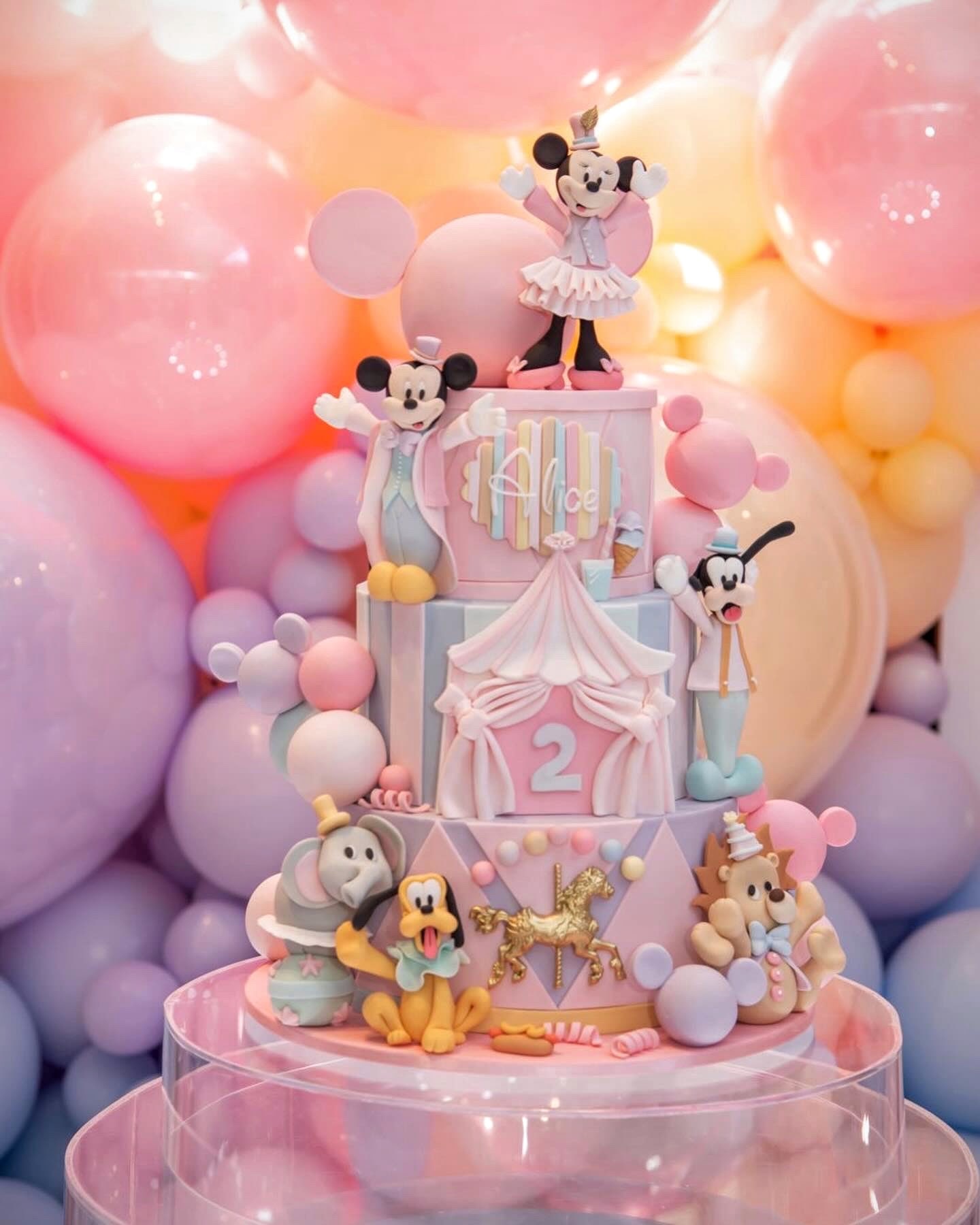 Bolo de aniversário de três andares em tons pastel com tema de circo, personagens modelados à mão e carrossel dourado