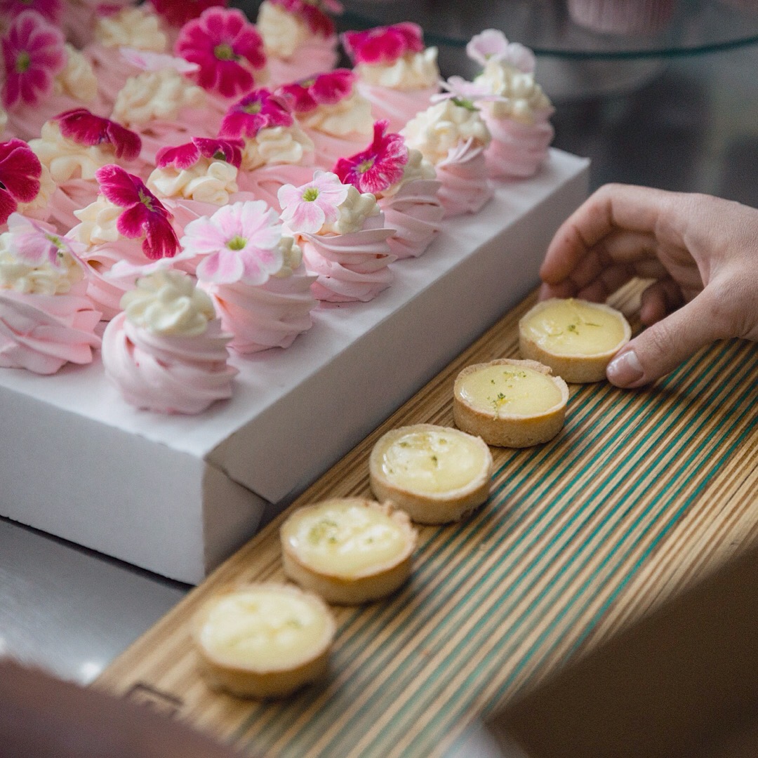Mini tortas de creme sobre bandeja de madeira ao lado de doces cor-de-rosa decorados com flores