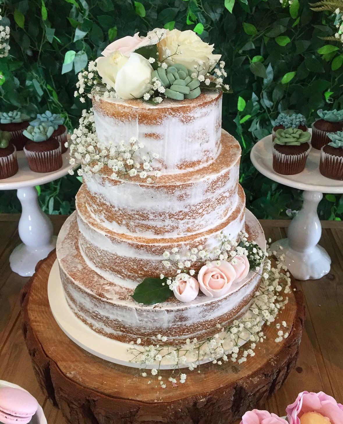 Naked cake de quatro andares com massa aparente e acabamento raspado, decorado com rosas brancas e cor de rosa, suculentas em açúcar e mosquitinhos, sobre base de tronco de madeira